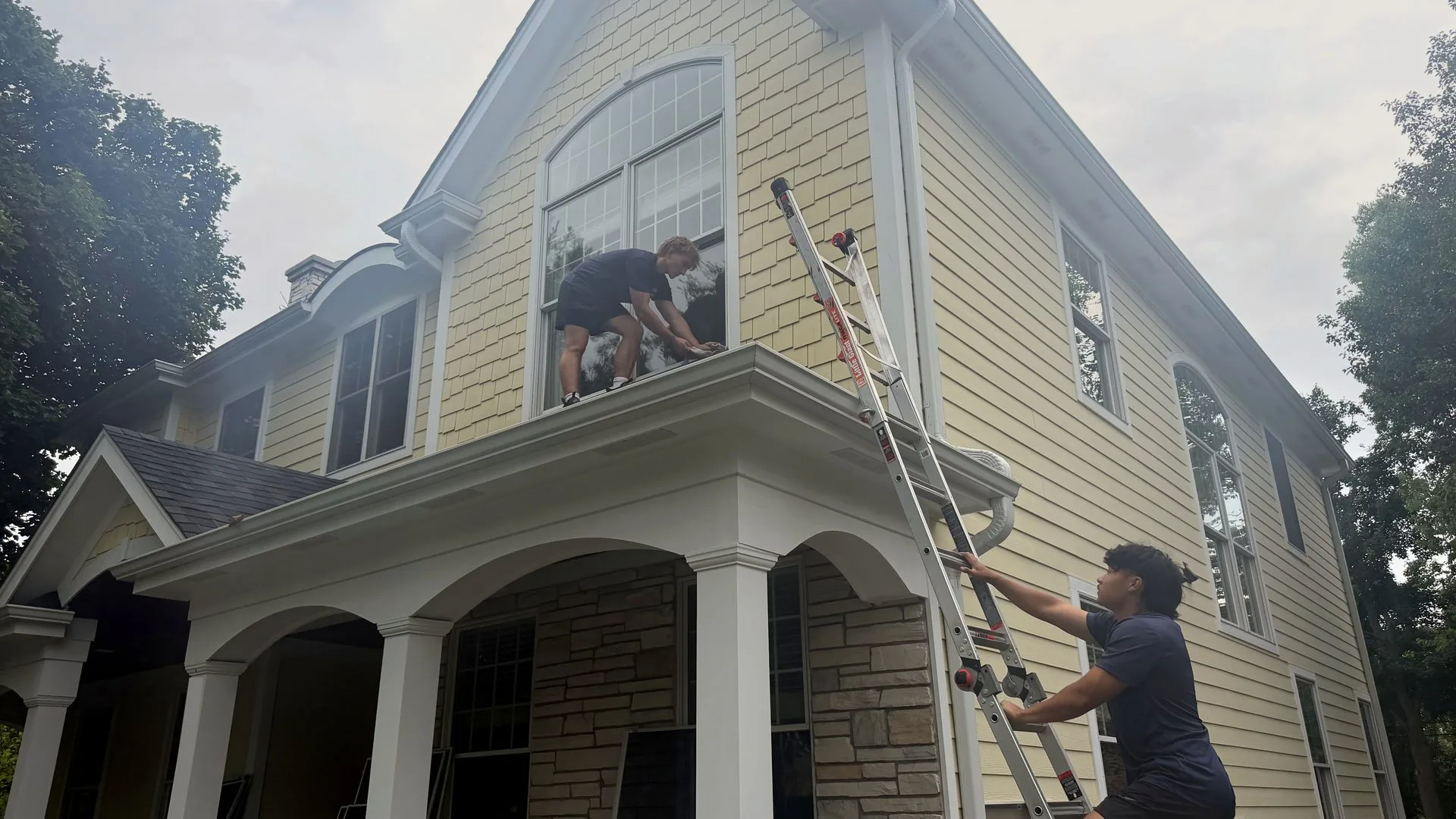 ClearDay technicians cleaning exterior windows on a yellow house in the Northwest Suburbs